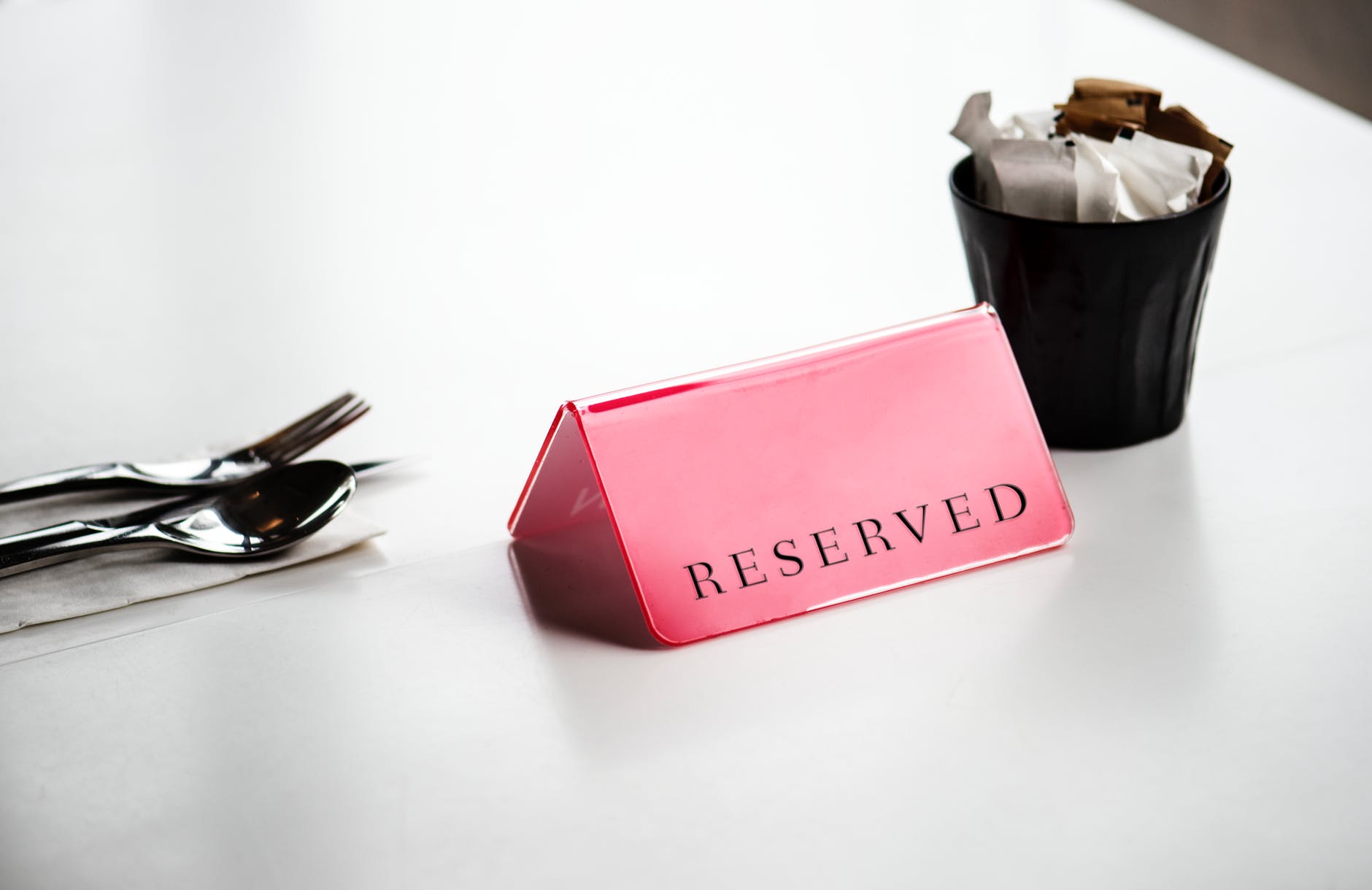 red reserved signage beside stainless steel spoon and fork on white surface